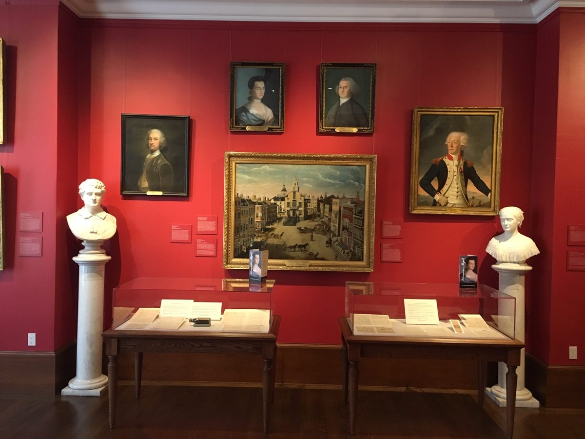 Two exhibit cases with wall paintings hanging above and a marble bust on either side